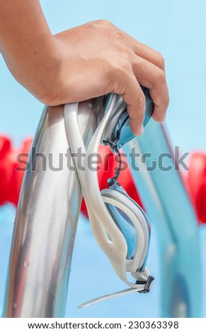 Close up the hand with swimming sport goggles grabs on metallic ladder bar, ready entrance to swimming pool.