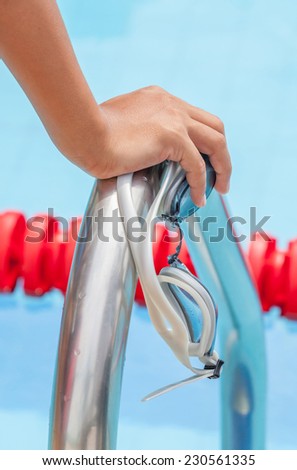 Start swimming race concept with closeup the hand grab on ladder bar with swimming goggles.