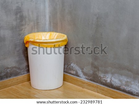 The white can bin at the corner on wooden floor with exposed cement background, for cleaning and recycle.