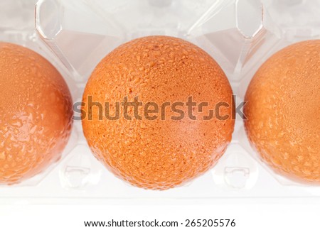High angel shot of brown eggs and water drops in plastic package on white background.