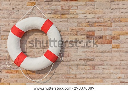 The life buoy is hanged on brick wall background nearby the swimming pool, for safety and rescue.