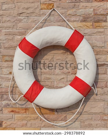 The white and red life buoy hanging on the brick wall around the swimming pool, for safety and rescue.