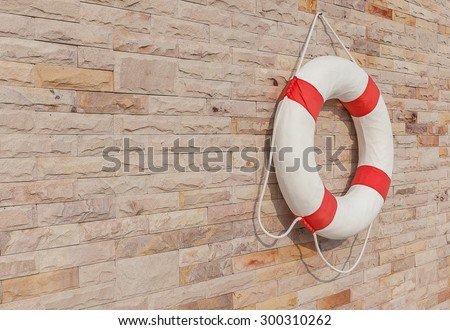 The white and red life buoy is hanging on the brick wall around the swimming pool, for safety and rescue.