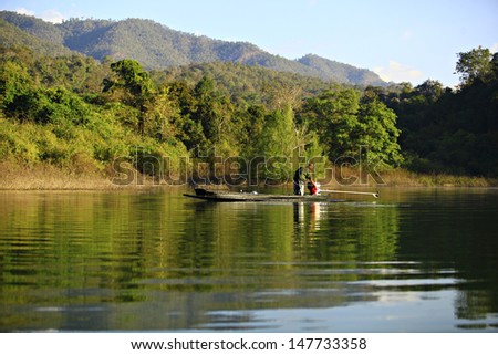 Young man catching Fish on wooden boat in Maengud Somboonchon Dam, Chaing mai Province, Thailand..