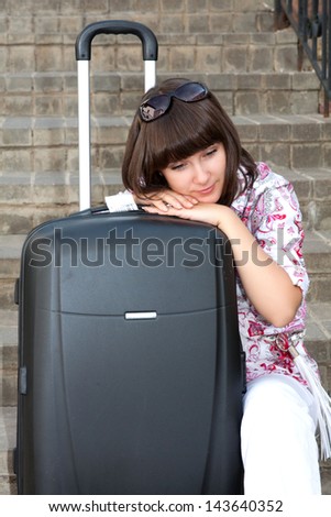 Beautiful girl sad sitting on the stairs with a suitcase