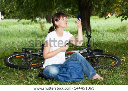 The girl on the lawn in the park corrects makeup