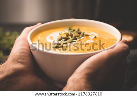 Bowl of warm pumpkin soup in hands. Holding bowl of vegan pumpkin soup. Comfort food. Toned image, selective focus