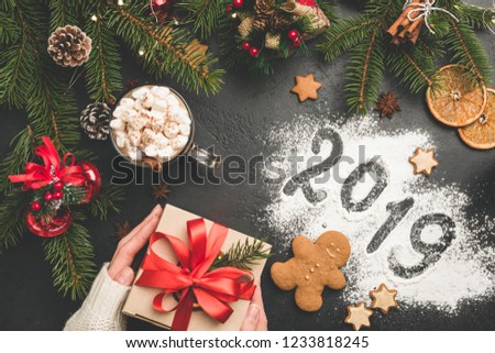 2019 Christmas or New Year background with gift box, fir tree, hot chocolate. 2019 written on flour on black concrete background. Festive Winter Holidays concept