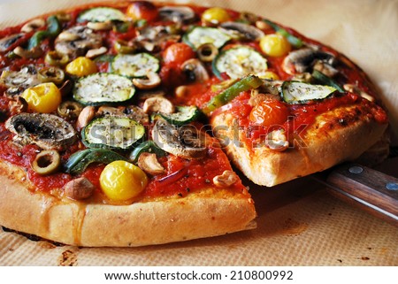 Vegan pizza with zucchini, mushrooms, cherry tomatoes, bell pepper, cashew nuts and olives