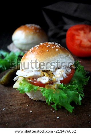 Homemade sandwich with shredded chicken, tomato, green salad, pickles, mustard and yogurt sauce on burger buns, black background