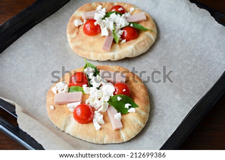 Mini pizza on pita bread with tomatoes, ham, white cheese and fresh basil leaves