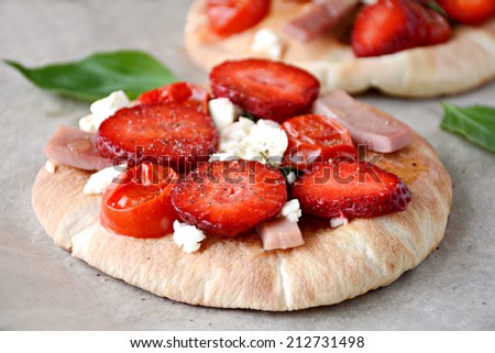 Small pizza on pita bread with tomatoes, ham, cheese and strawberries, close up