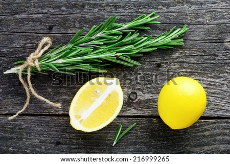 Fresh rosemary springs and lemons on gray wooden table, close up. Natural food and herbs background