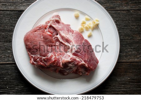 Fresh meat steak on round plate with chopped garlic, cooking ingredients. Above