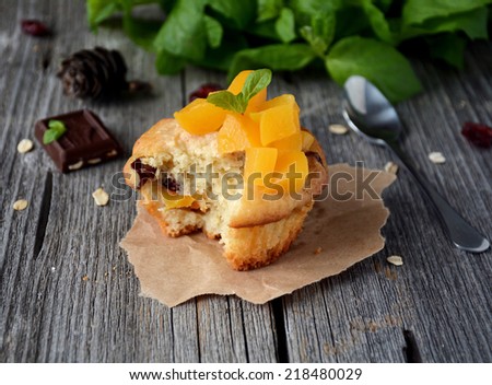 Cupcake with cranberries topped with peaches and mint leaf on wooden table top