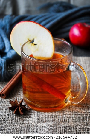 Spiced apple cider in glass cup with cinnamon stick, star anise decorated with fresh apple slice. Seasonal hot drink
