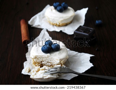 Two small cheesecakes topped with blueberries on dark wooden table