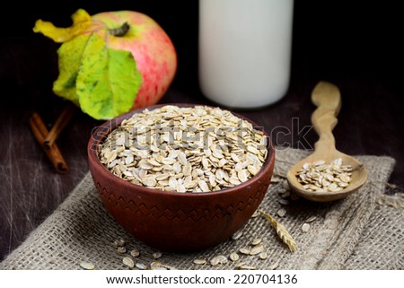 Rolled oats in bowl with bottle of milk, wooden spoon and wheat ear on linen. Horizontal healthy food still life