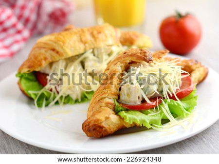 Gourmet sandwich: croissant with chicken avocado ceasar salad and grated cheese on white plate, close up