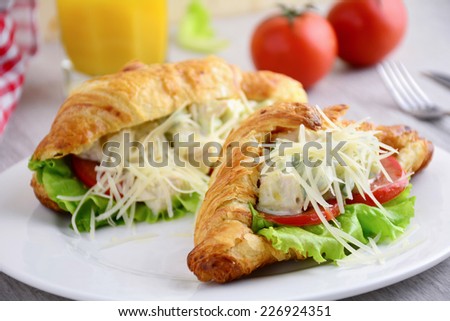 Gourmet sandwich: croissant with chicken, tomato, avocado and cheese salad on white plate, close up