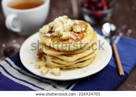 Pancakes topped with banana and coconut, cup of green tea and cranberries on kitchen cloth on wooden table. Breakfast image