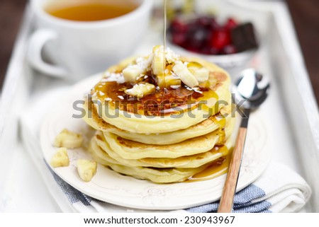 Breakfast on a tray: cup of green tea and stack of pancakes with banana slices and coconut flakes on vintage plate on brith white and blue kitchen towel