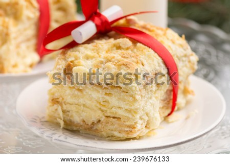 Piece of Napoleon cake for Christmas with red ribbon, candle and small scroll with Christmas wishes, close up