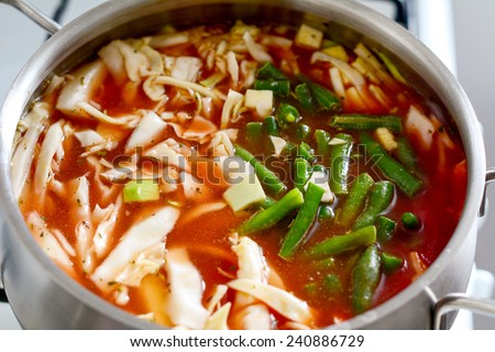 Vegetarian tomato vegetable soup with cabbage and green beans in pot, cooking process