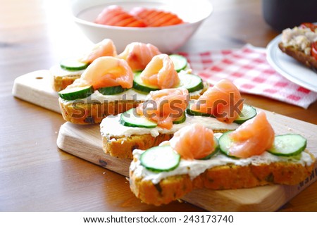 Toasts with cream cheese, sliced cucumber and smoked salmon on wooden board, breakfast close up