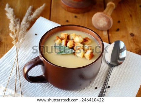 Potato cream soup with croutons garnished with sage leaf in brown soup bowl on wooden table