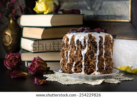 Chocolate gingerbread cake topped with yogurt sauce, fresh raspberries and blueberries with dried flowers and books around, home food still life
