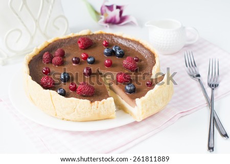 Chocolate cheesecake decorated with raspberries and blueberries on white plate on pink napkin with slice cut out. Bright sweet food image