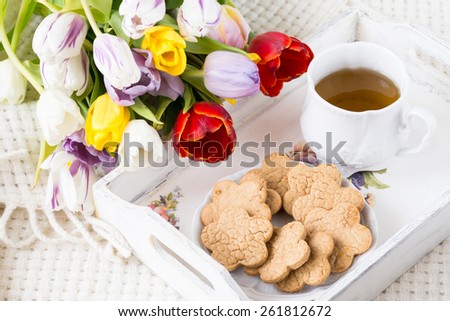 Breakfast in bed: homemade cookies, black tea and variety of colorful tulips on white tray. Close up