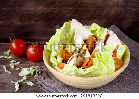 Healthy salad with hard boiled egg, cherry tomatoes, lettuce salad and grilled chicken breast drizzled with balsamic vinegar sauce in wooden bowl on brown napkin on brown table