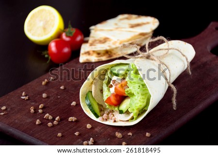 Tortilla wraps with fresh cucumber, tomatoes, lettuce leaf and grilled chicken breast on wooden cutting board. Healthy lunch, snack or light dinner meal