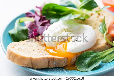Whole wheat toast with poached egg, runny egg yolk and fresh green salad leaves. Close up healthy food image
