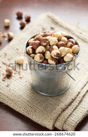 Hazelnuts in small metal bucket on linen on wooden table, close up raw healthy food