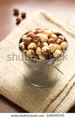 Hazelnuts in small metal bucket on linen on wooden table, close up raw healthy food. Warm tones