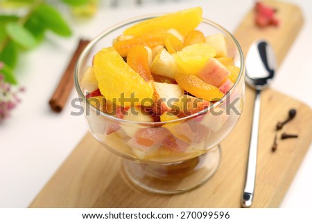 Fresh fruit salad with pear, apple, orange and banana in dessert cup on wooden cutting board, white background. Close up. Colorful image