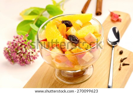 Fresh fruit salad with pear, apple, orange, raisins and banana in dessert cup on wooden cutting board, white background. Close up. Colorful image