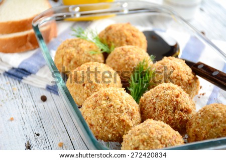 Fish balls baked in glass dish garnished with dill on white and blue napkin served with slice of white bread and lemon