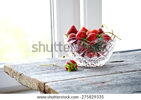 Fresh organic strawberries in crystal bowl on wooden table near window