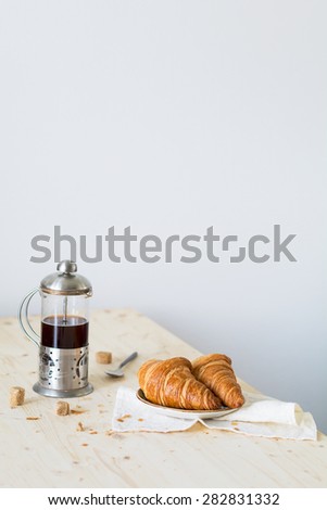 Croissants and coffee in french press on wooden table