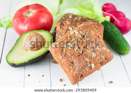 Fresh vegetables and whole wheat bread with seeds on white table, close up