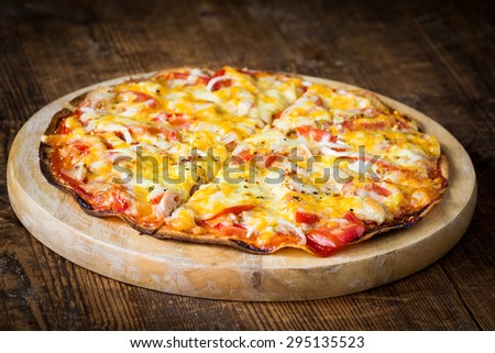 Homemade thin crust pizza fresh from the oven on round wooden board