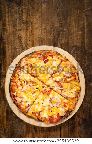 Homemade thin crust pizza fresh from the oven on round wooden board, top view