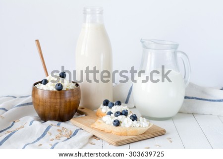 Assortment of dairy products: bottle of milk, yogurt, farmers cheese, toast with curd and blueberries on white board