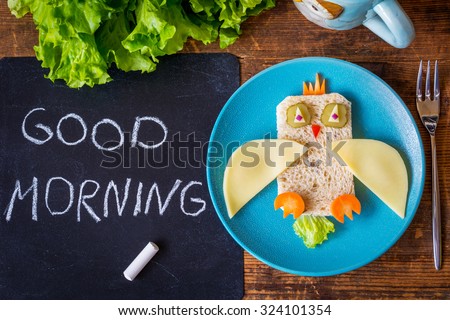 Funny sandwich owl for kids on plate, black chalkboard with Good morning greeting. healthy breakfast. Wooden table background,