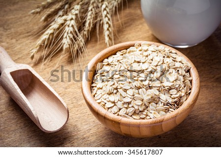 Rolled oats (oat flakes), milk and golden wheat ears on wooden background. Raw food ingredients, healthy lifestyle, cooking food
