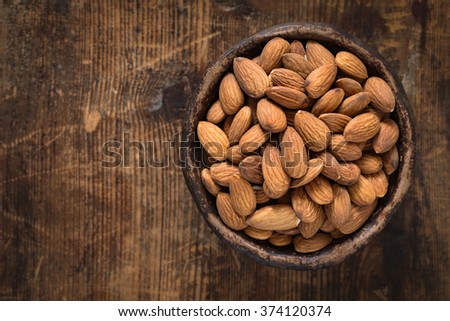 Almonds in brown bowl on textured wooden background, top view. Copy space on left side